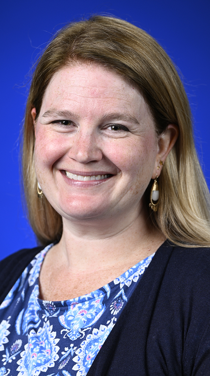 Headshot of a woman wearing a dark blue sweater over a blue patterned blouse.