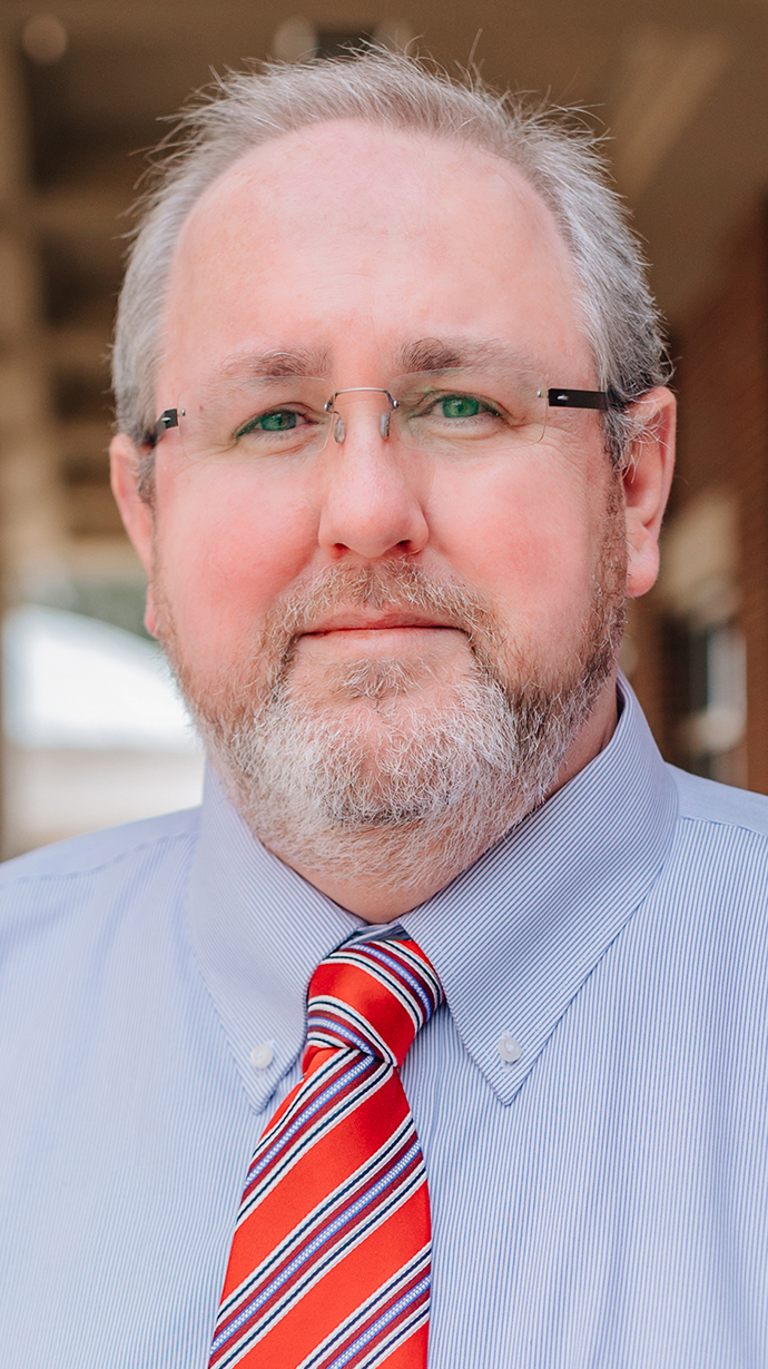 Headshot of a man wearing a blue shirt and a red striped tie.