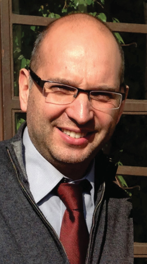Headshot of a man wearing glasses in front of an outdoor arbor.
