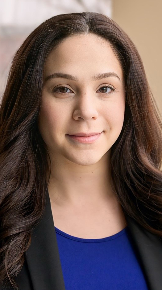 Headshot of a woman wearing a black jacket over a purple blouse.