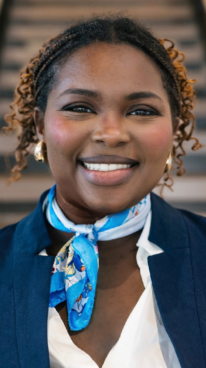Headshot of a young woman wearing a navy blue blazer and a light blue scarf over a white blouse.