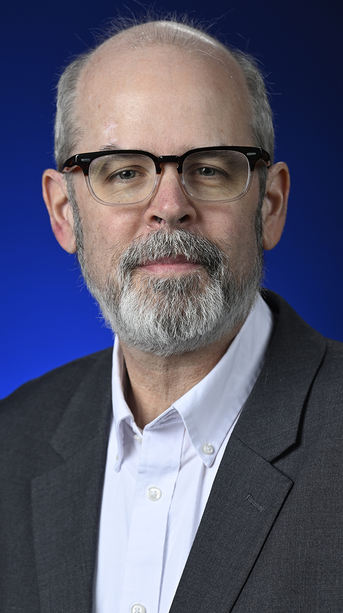 Headshot of a man wearing a dark gray jacket over a white buttoned shirt.