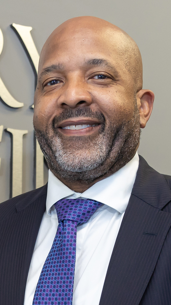 Headshot of a man wearing a dark suit and a purple tie.