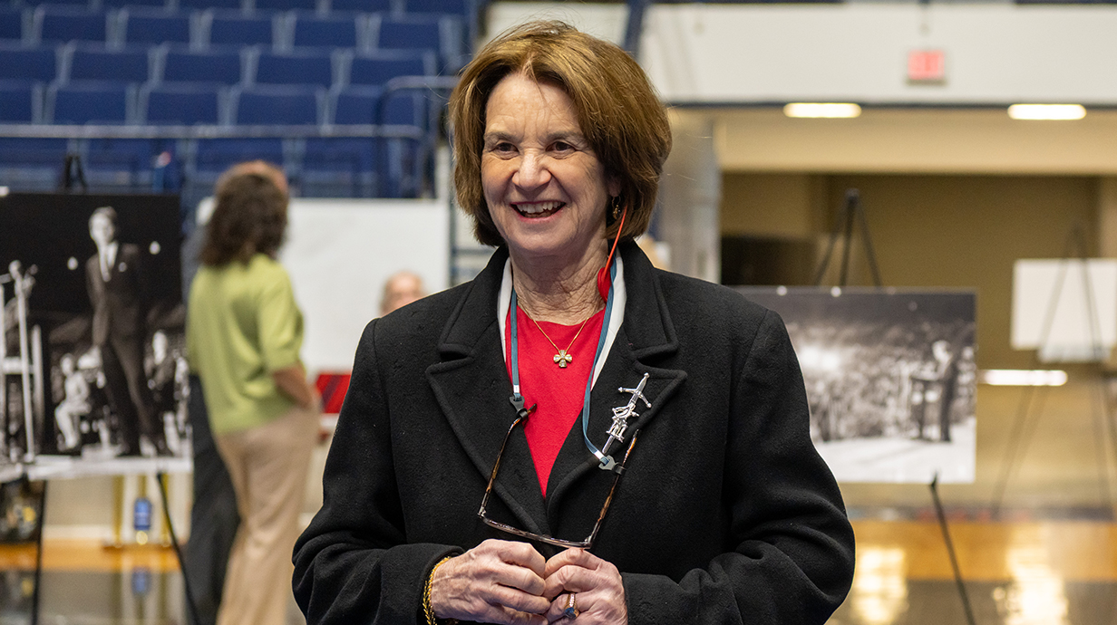 A woman wearing a blue blazer stands in a basketball arena.