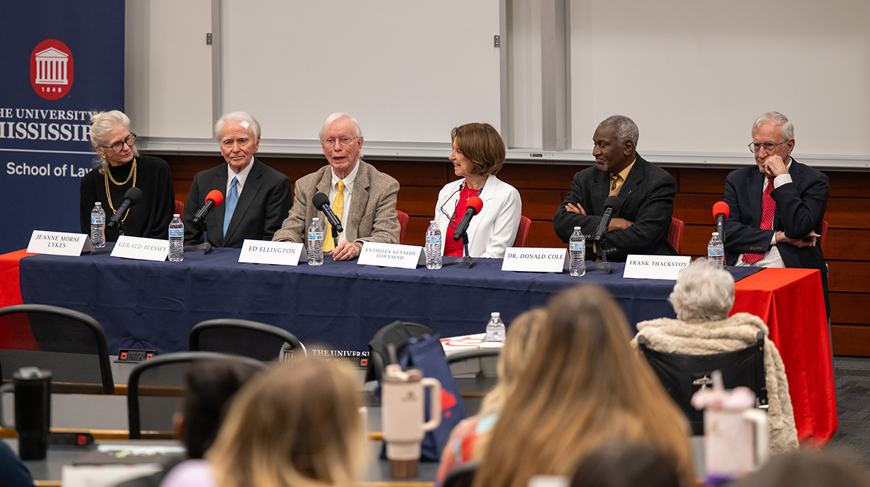 Six people sit at a table at the front of an auditorium.