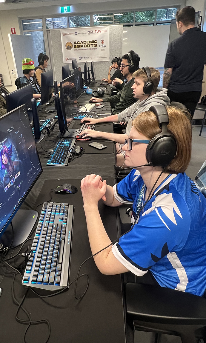 A young woman sits at a computer with a line of other people at computers behind her.