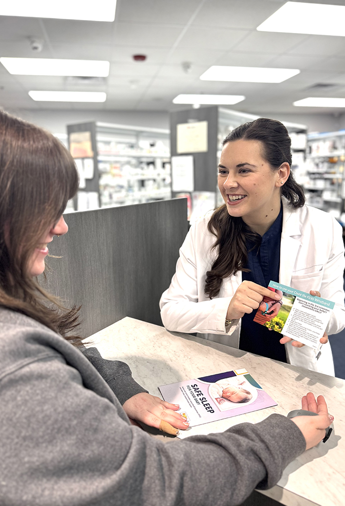 A pharmacist wearing a white coat talks with a patient at a pharmacy counter.