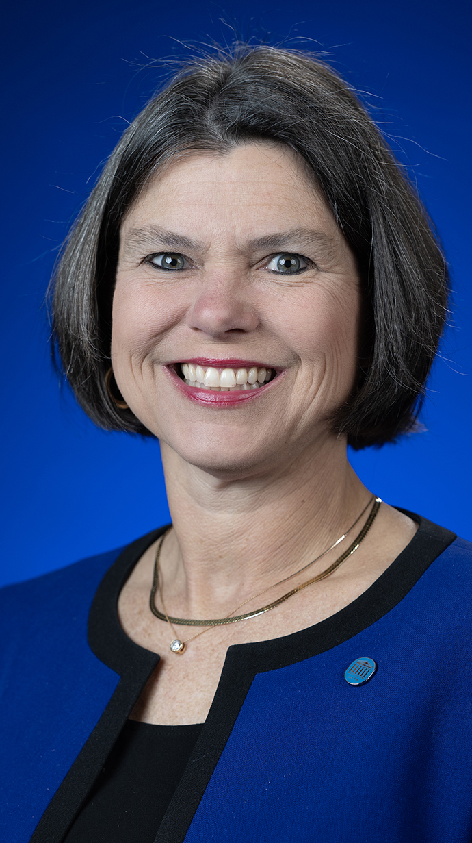 Headshot of a woman wearing a blue jacket over a black blouse.