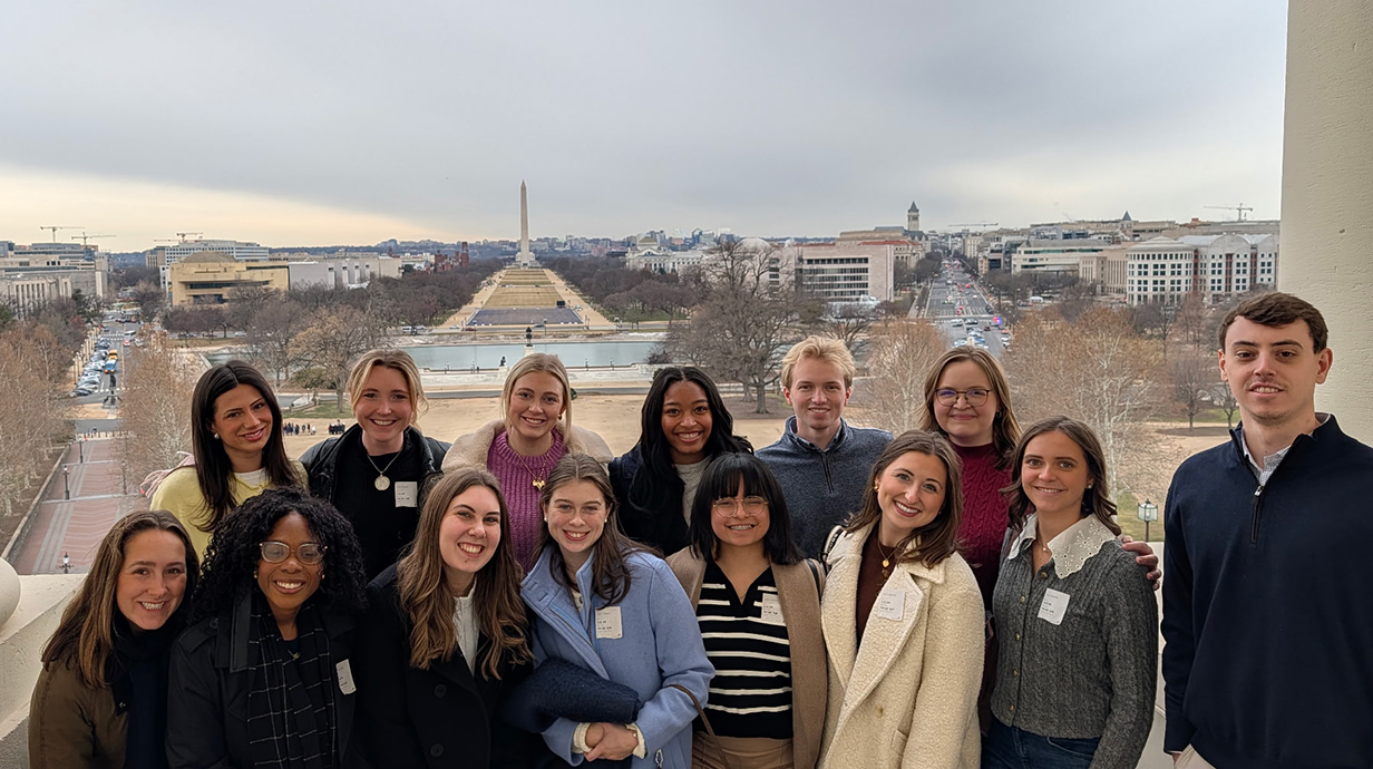 A group of young people stands on the steps of the U.S. Capitol, with the National Mall behind them.