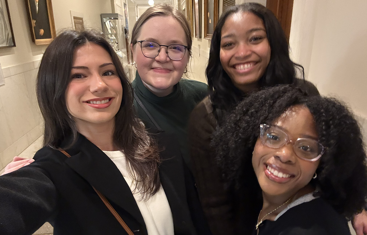 Four young women talk a selfie in an office hallway.