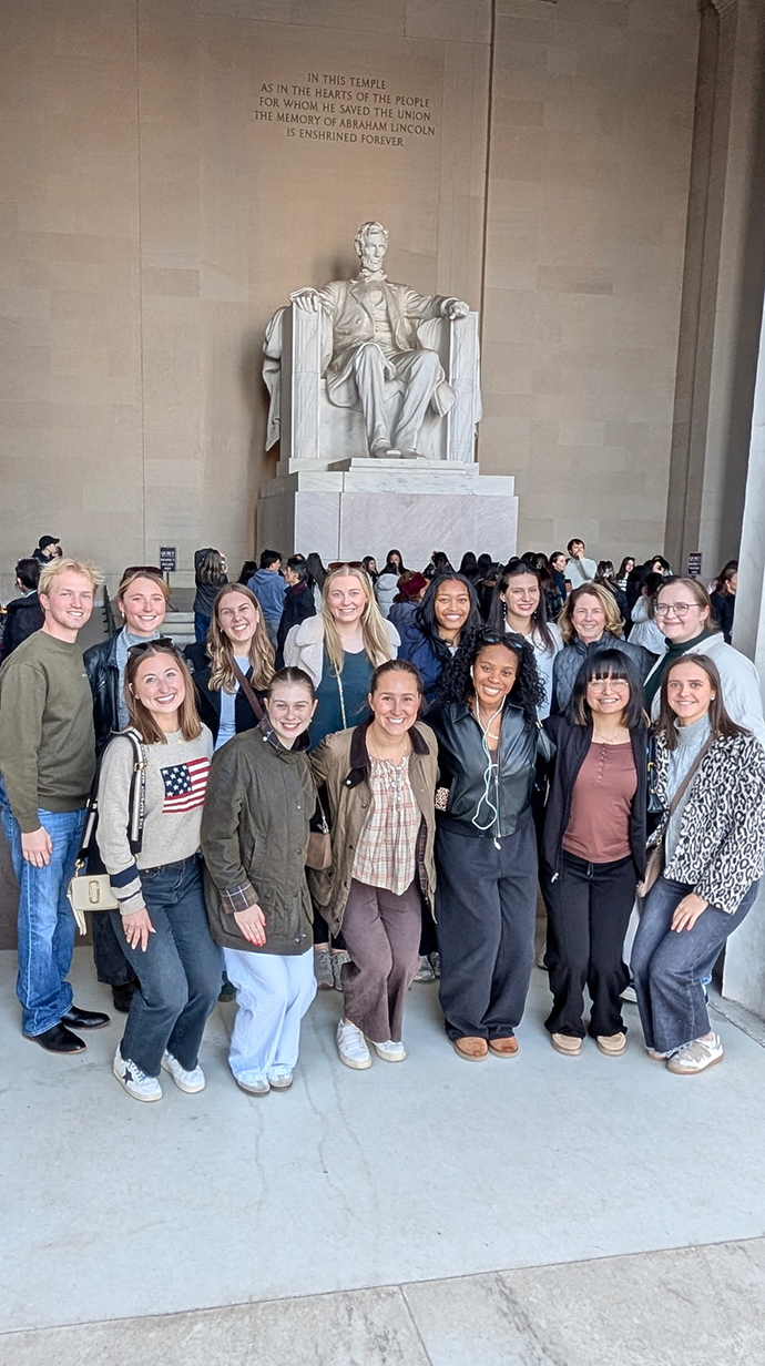 A group of young people stands inside the Lincoln Memorial.