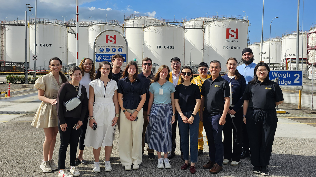 A group of young people stand in front of a chemical processing facility.