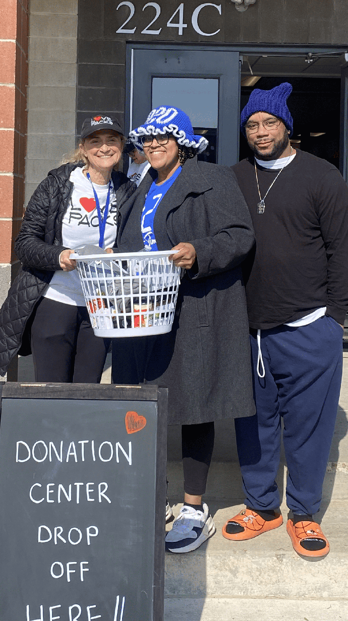 Two women and a man hold a basket of items at a donation drop-off site.