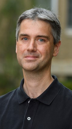 Headshot of a man wearing a dark polo shirt and standing outdoors.