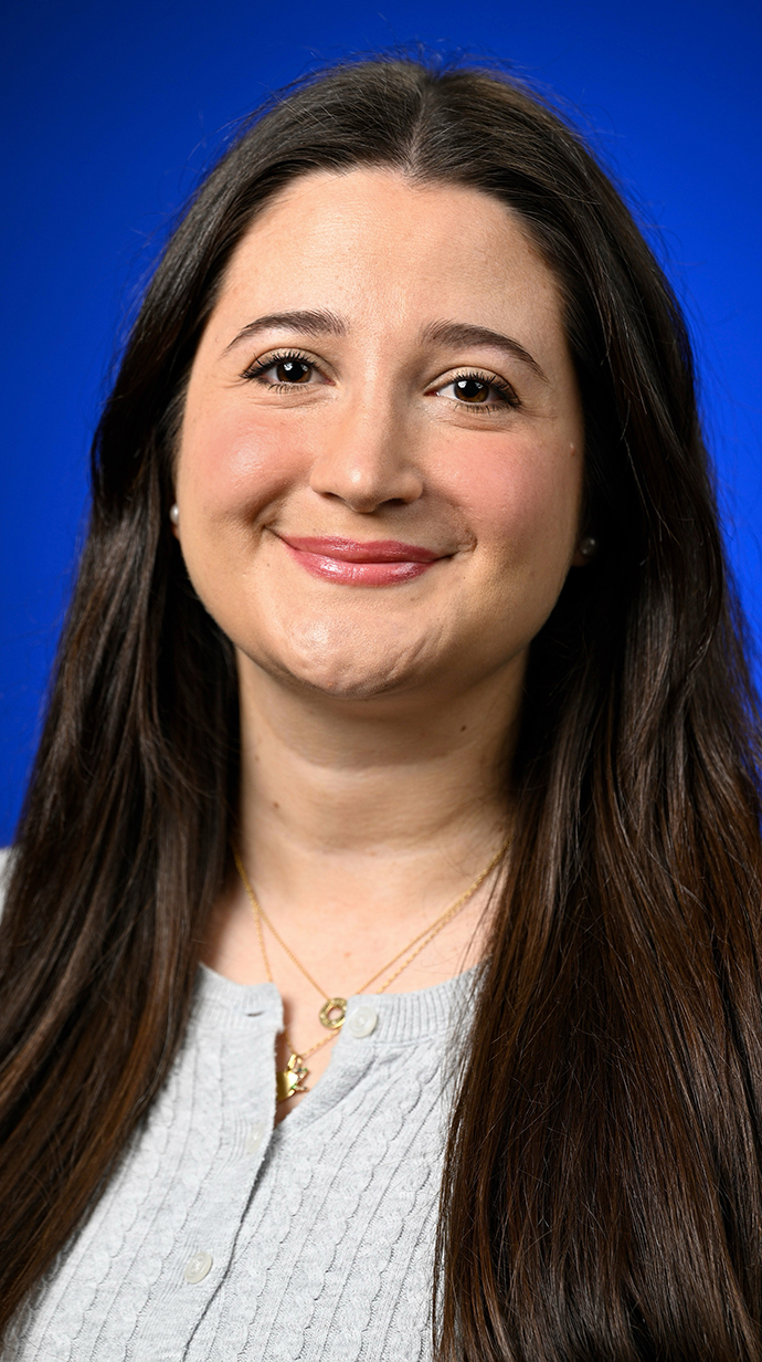 Headshot of a woman with long brown hair wearing a gray sweater.