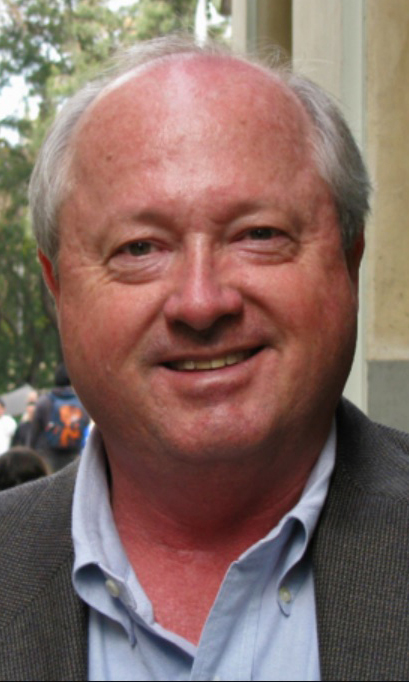 Headshot of a man wearing a gray jacket over a light blue shirt.