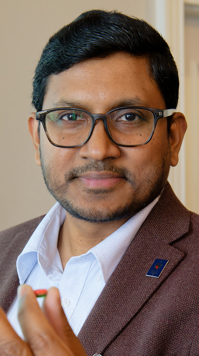 Headshot of a man wearing a brown jacket and a white shirt.