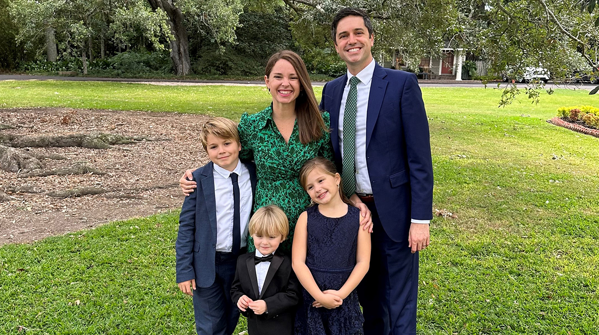 A woman, a man and three small boys pose for a family photo outdoors.