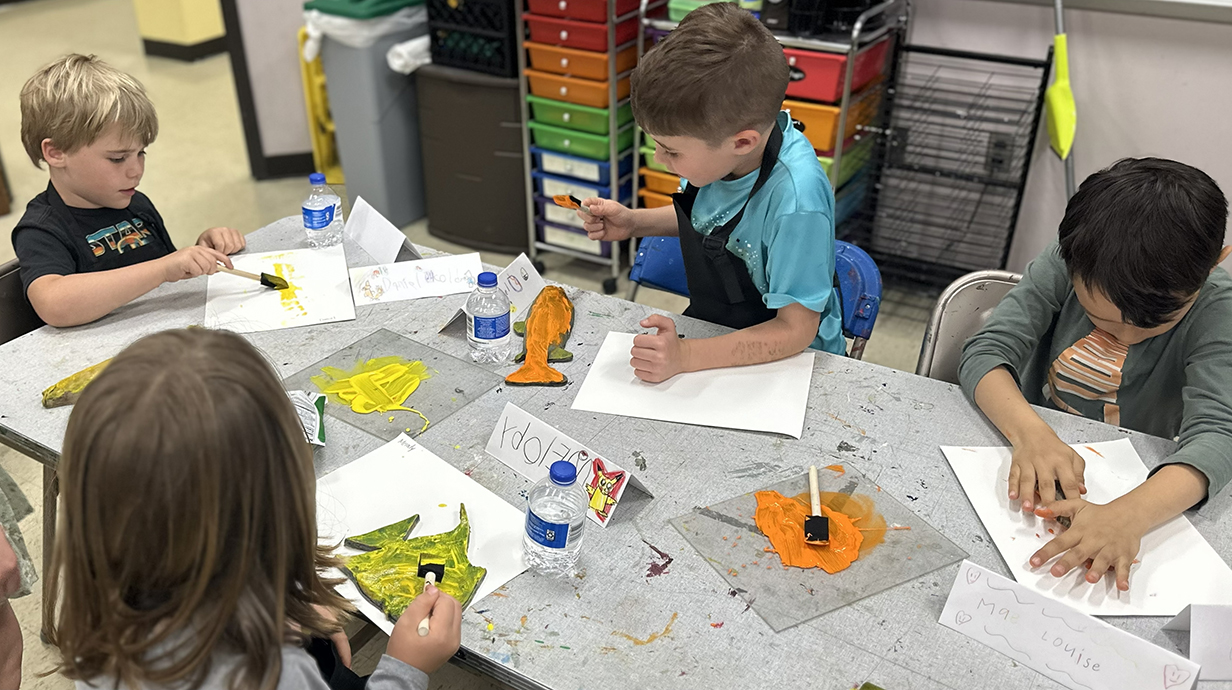 Children seated around a paper-covered table practice painting.