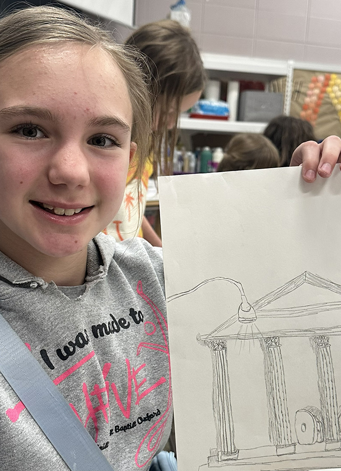 A young girl displays a drawing.