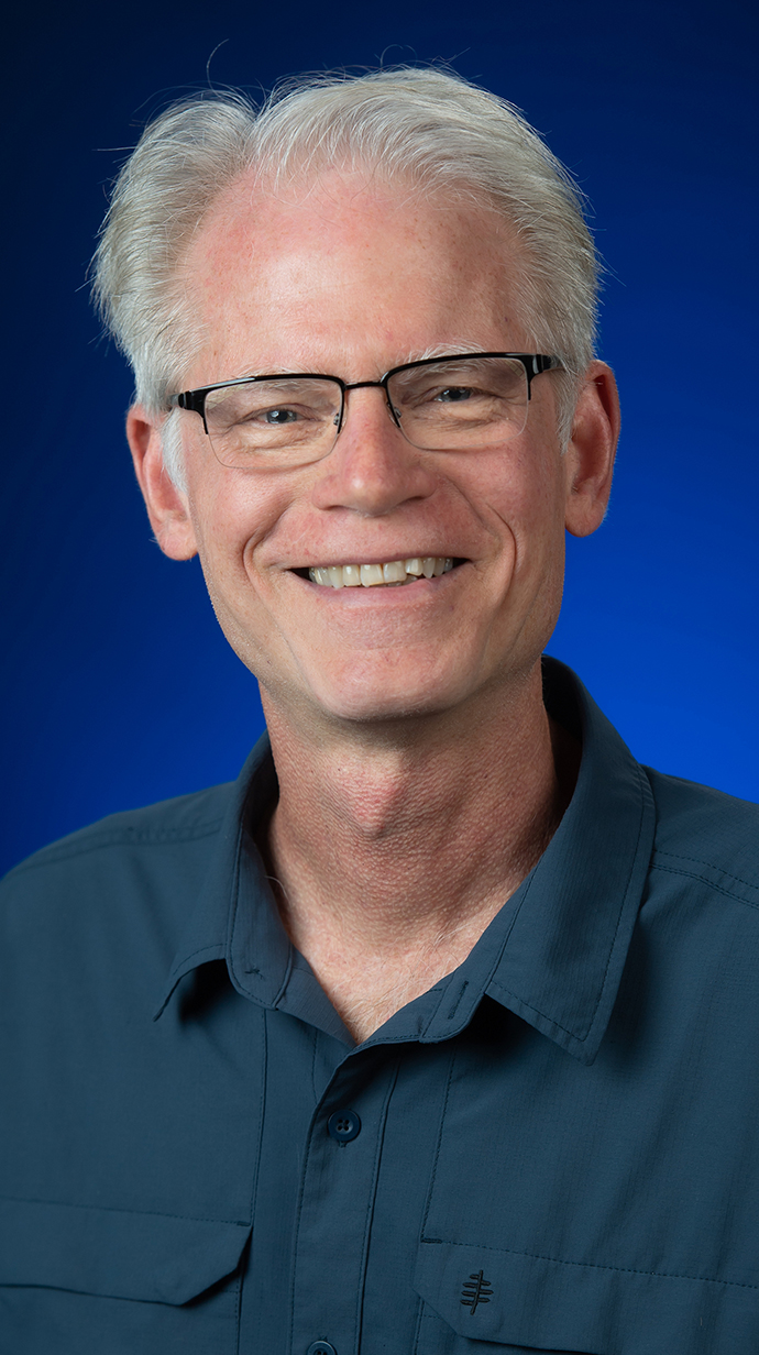 Headshot of a man wearing glasses and a casual blue-green shirt.