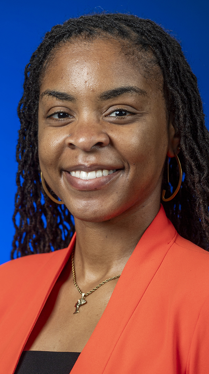Headshot of a woman wearing a coral jacket over a black blouse.