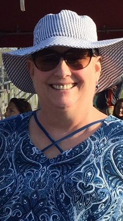 Headshot of a woman wearing a floppy white hat and sunglasses on a sunny day.