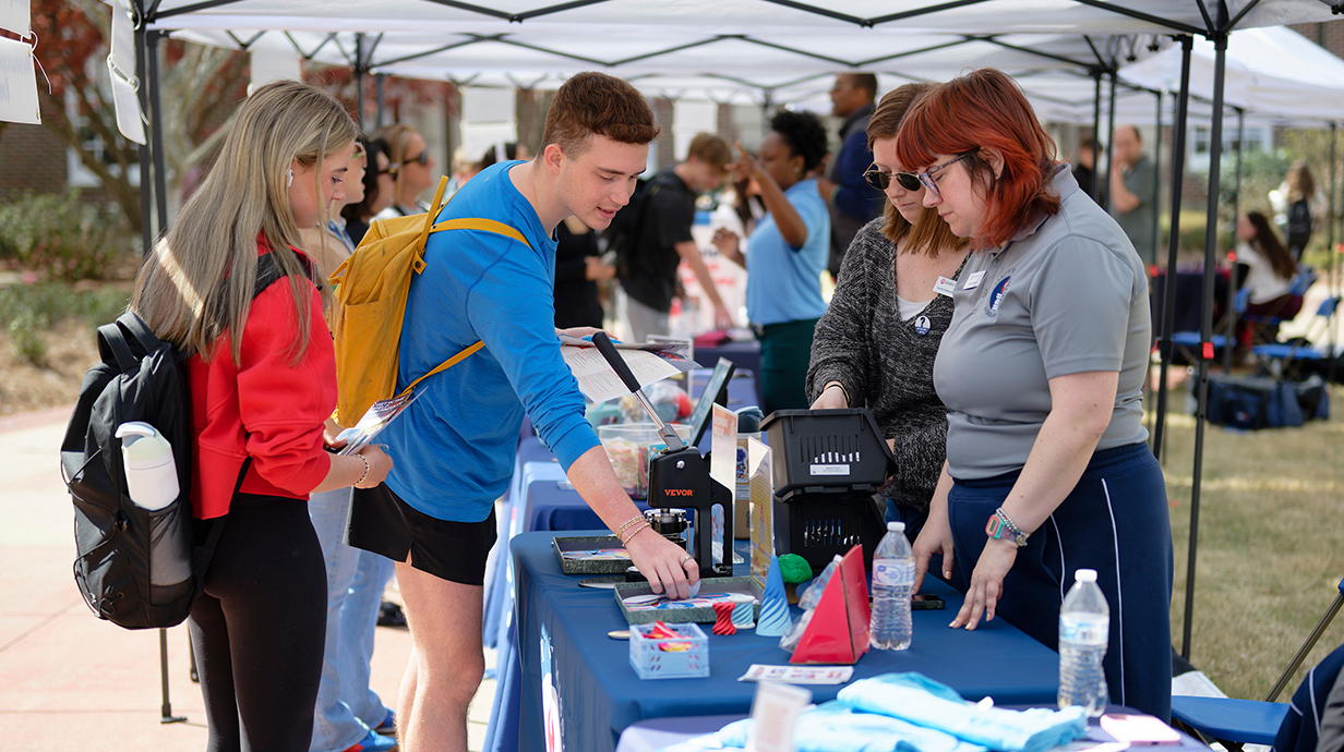 A young woman and young man check out materials displayed on a table at an outdoor activity fair.