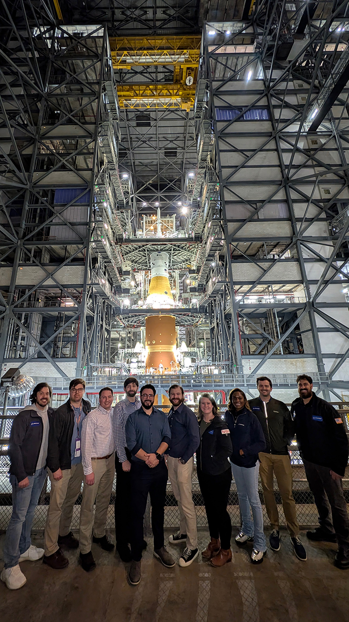A group of people stand in front of a rocket being assembled at the Kennedy Space Center.