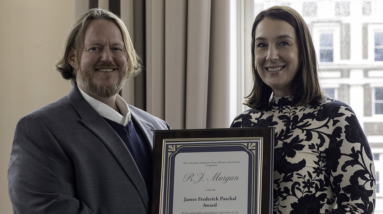A woman presents a man with a framed award certificate.