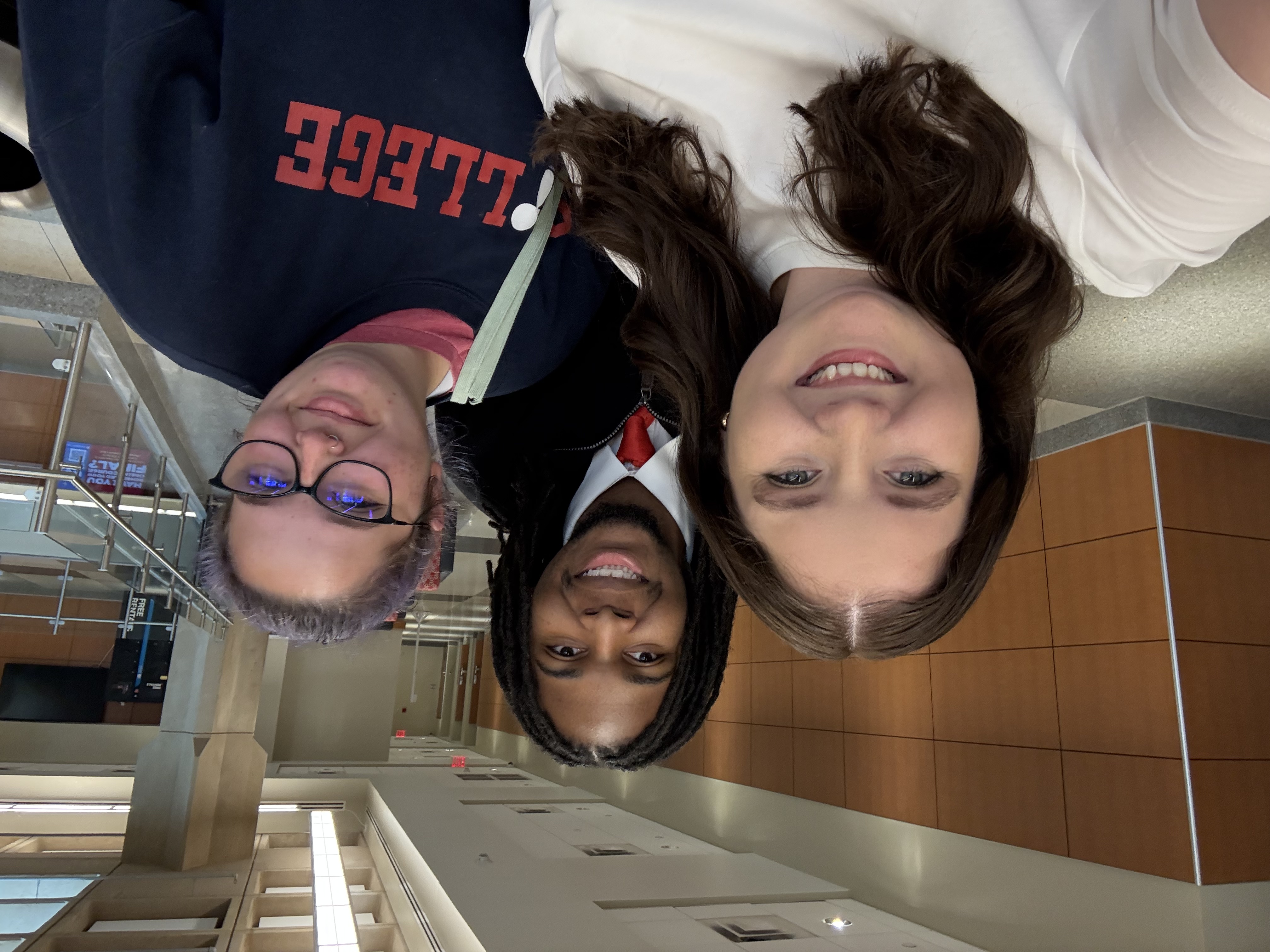 A young man and two young women take a selfie in a large building lobby.
