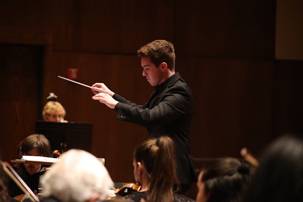 Donahue conducts an orchestra with a baton.