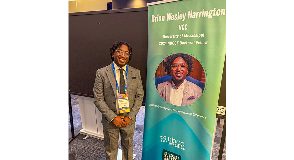 Brian Harrington stands in front of a banner announcing his doctoral fellowship.
