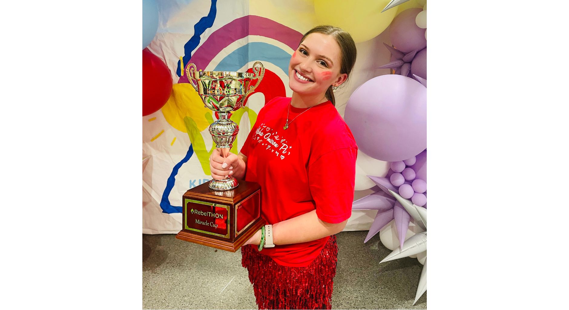 A young woman wearing a red T-shirt holds a large trophy.