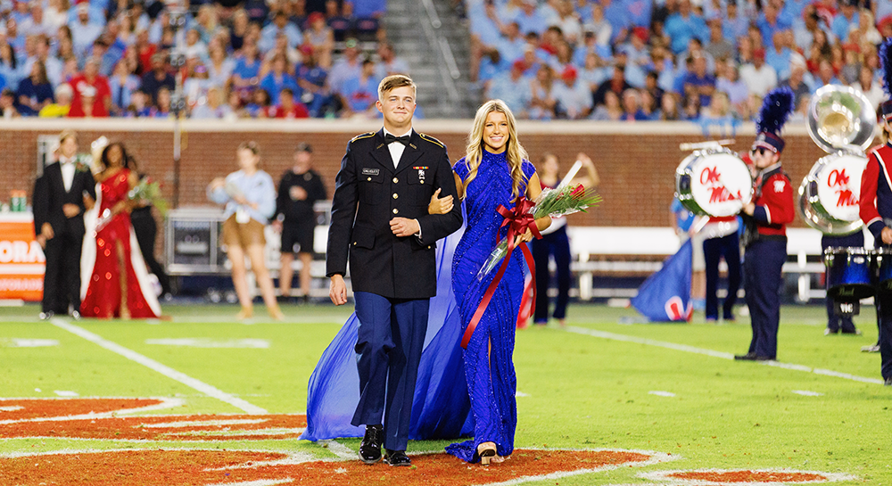 Collins walks on a football field in a gown escorted by a fellow student.