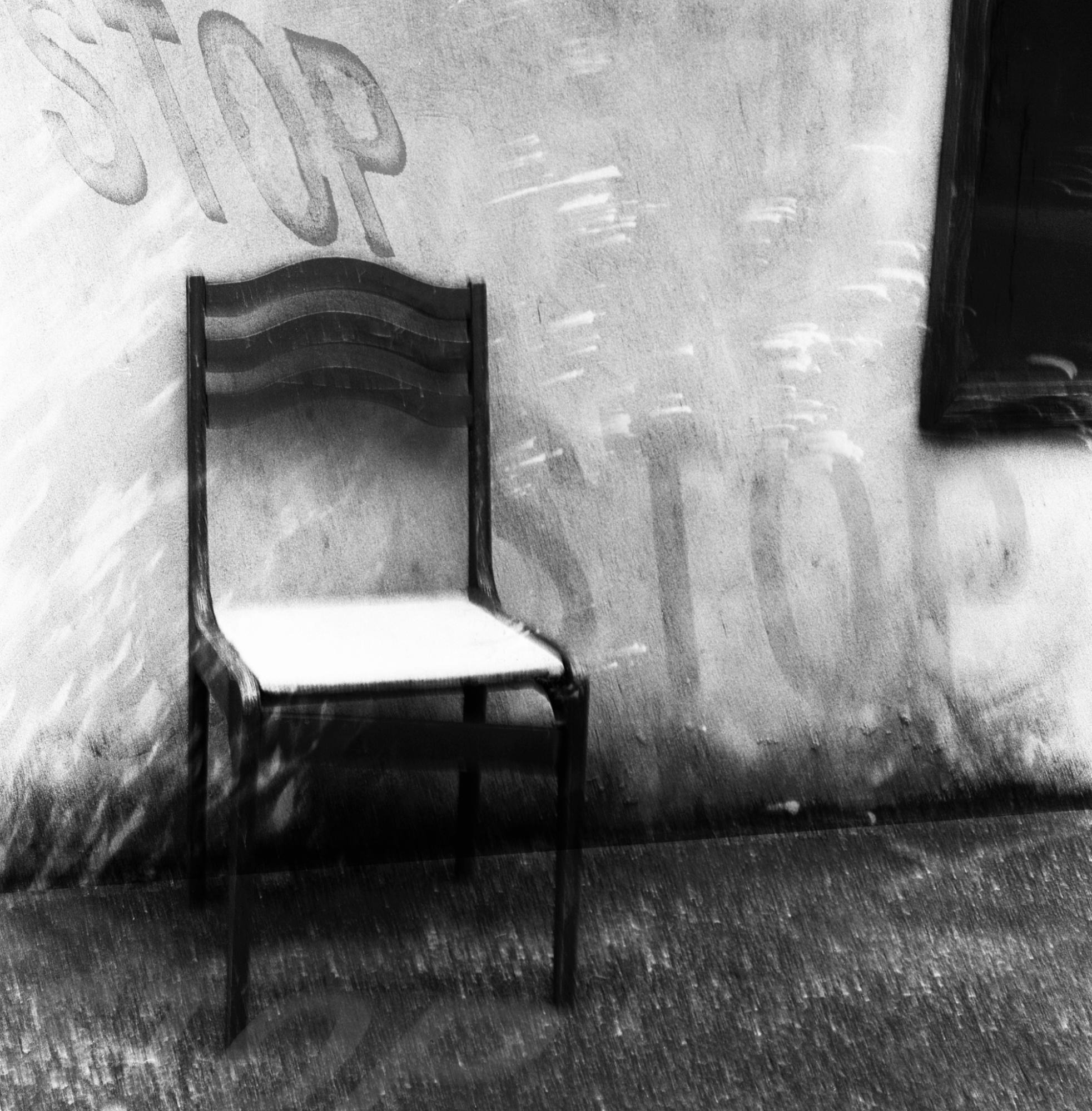 A black-and-white artistic photo of a chair sitting against a wall.