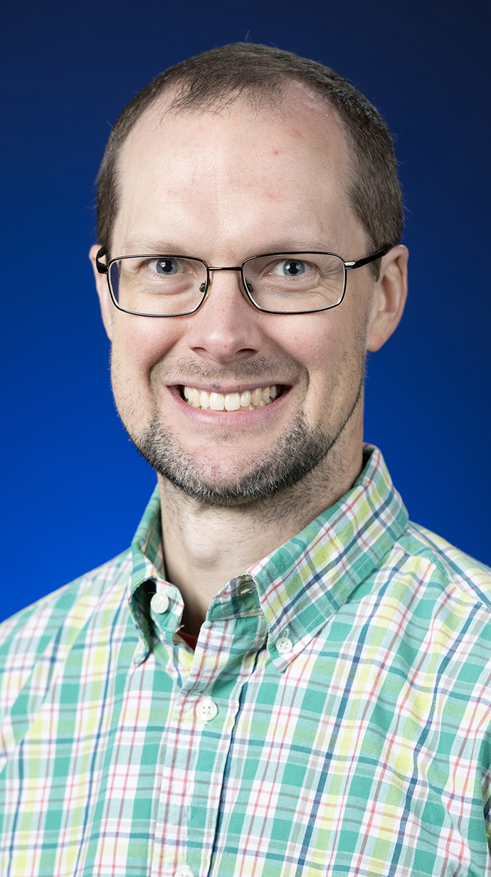 Headshot of a man wearing glasses and a green plaid shirt.