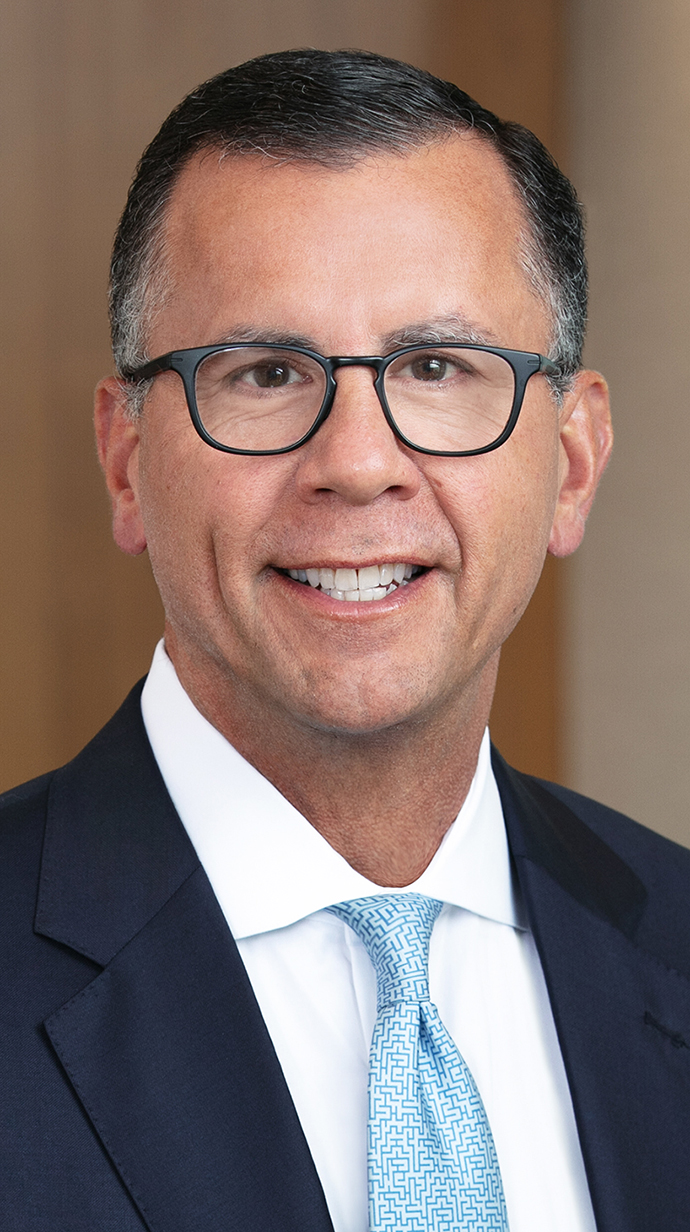 Headshot of a man wearing glasses and a dark suit with a light blue tie.