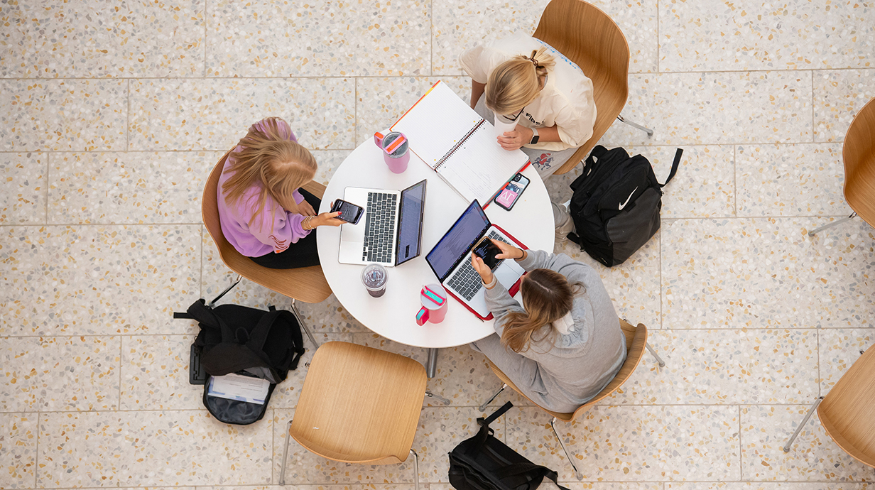 An overhead photo of three young women with laptops sitting at a round table.