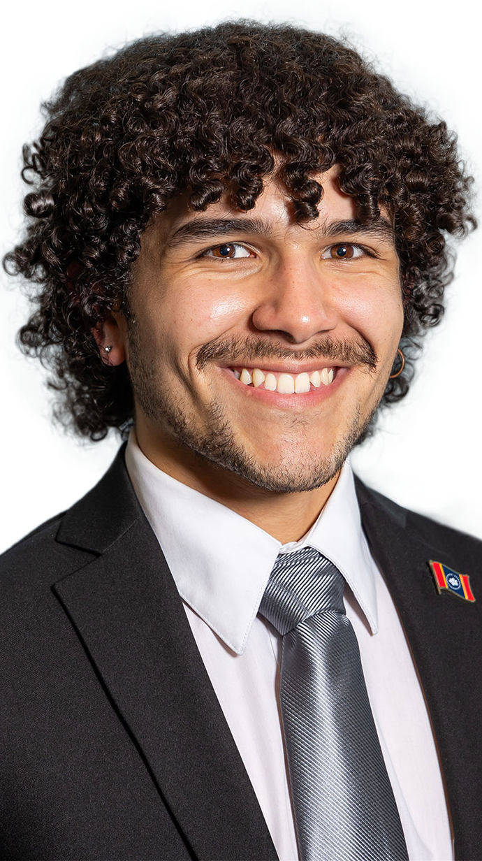 Headshot of a young man wearing a dark suit with a Mississippi state flag lapel pin.