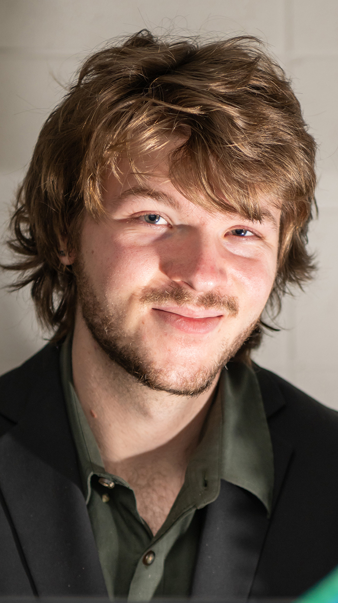 Headshot of a young man wearing a black jacket and dark shirt.