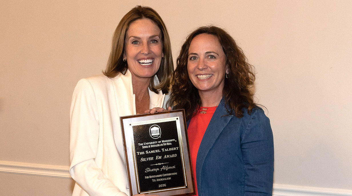 A woman presents another woman with an award plaque.