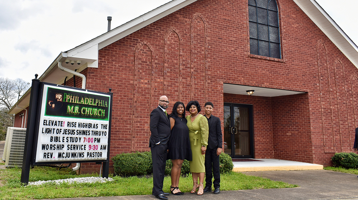 A family stands on a sidewalk in front of a brick church.