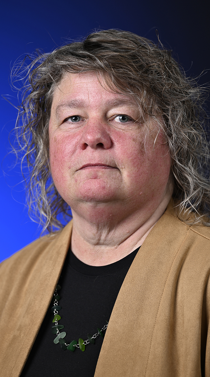 Headshot of a woman wearing a tan jacket over a black blouse.