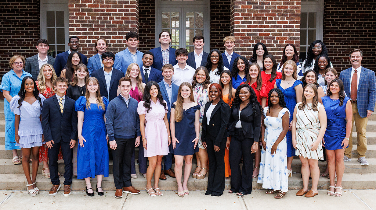 A large group of young people stands on the steps of a large brick building.