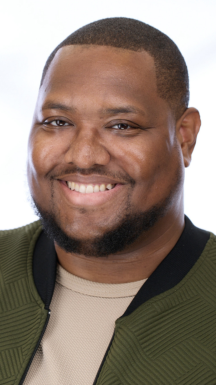 Headshot of a man wearing an olive jacket over a tan T-shirt.