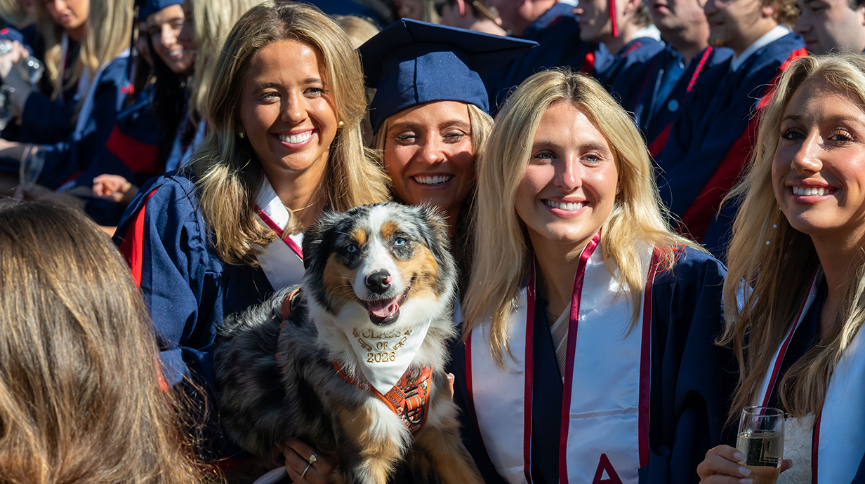 Four young women sit with a dog at a graduation ceremony.