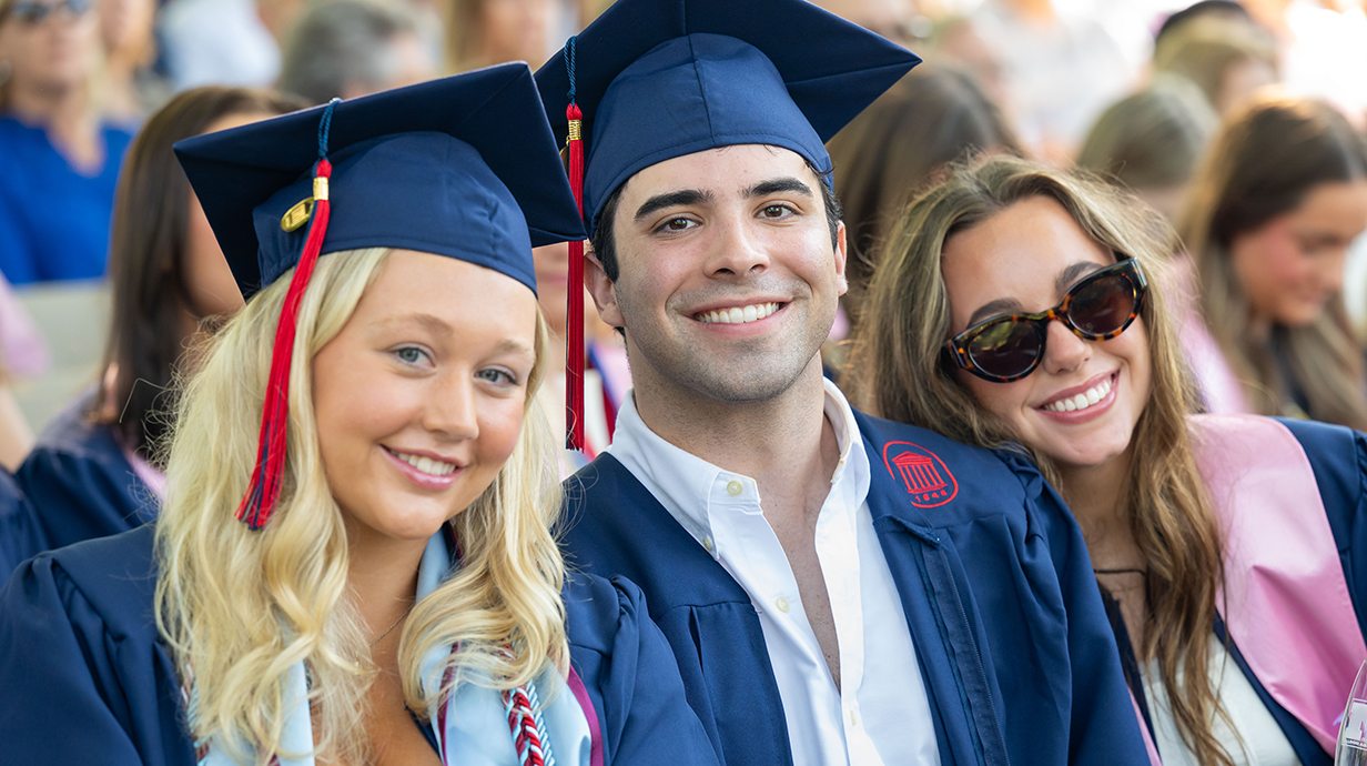 Two young women and a young man, all wearing graduation robles, pose for a casual photo.