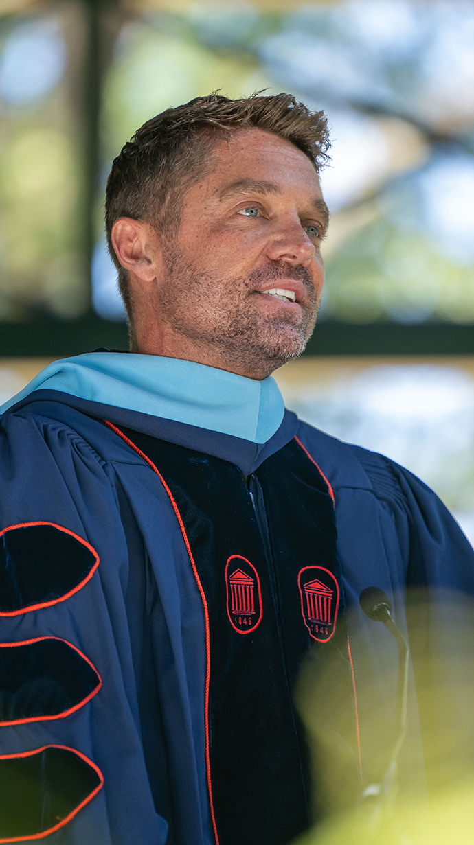 A man wearing graduation robes speaks at a podium.
