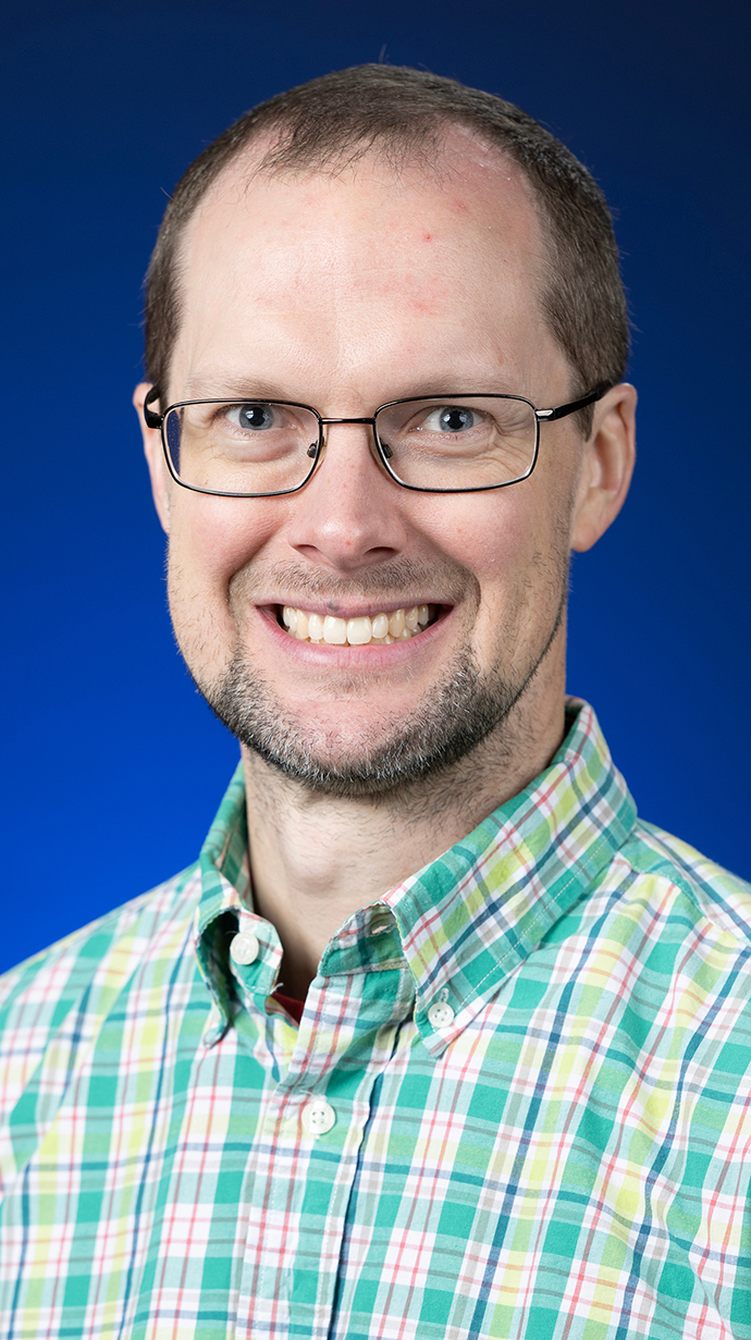 Headshot of a man wearing a green plaid shirt.